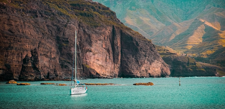 Segelschiff vor der steilen Felsküste Gran Canarias auf türkisfarbenem Wasser.